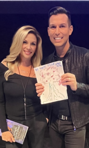 Psychic medium Matt Fraser smiling on stage at The Wiltern in Los Angeles while holding a fan drawing made for him by 9-year-old Zuma.